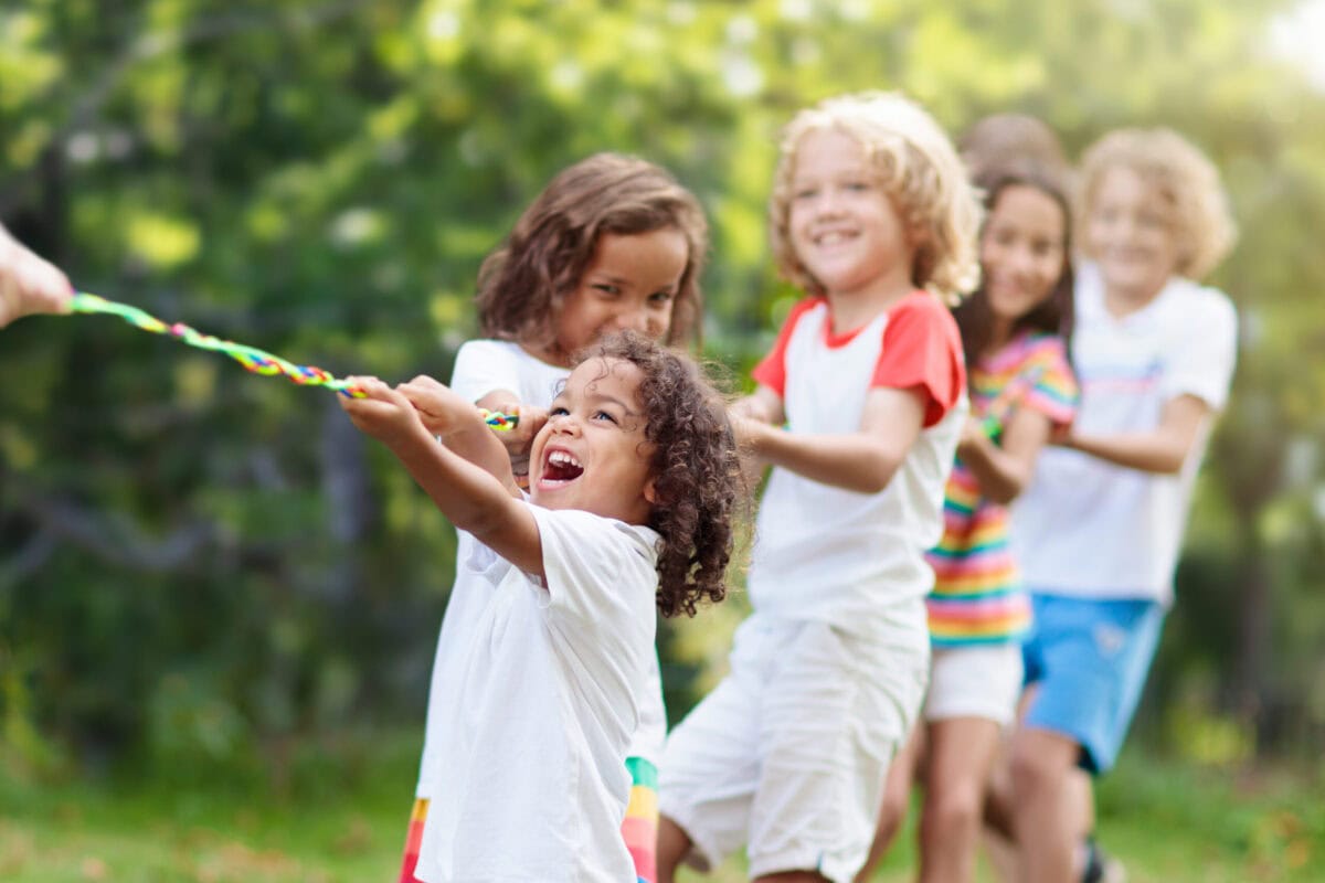 Kids play tug of war. Children pull rope. Kids play tug of war in sunny park. Summer outdoor fun activity. Group of mixed race children pull rope in school sports day. Healthy outdoor game for little boy and girl.
